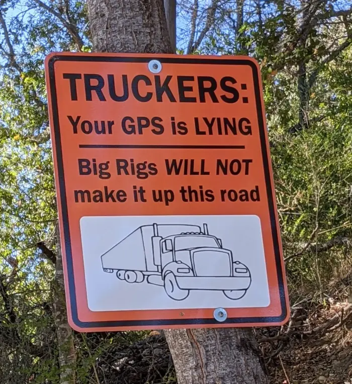 An orange traffic sign that says" TRUCKERS; Your GPS is LYING. Big Rigs WILL NOT make it up this road.