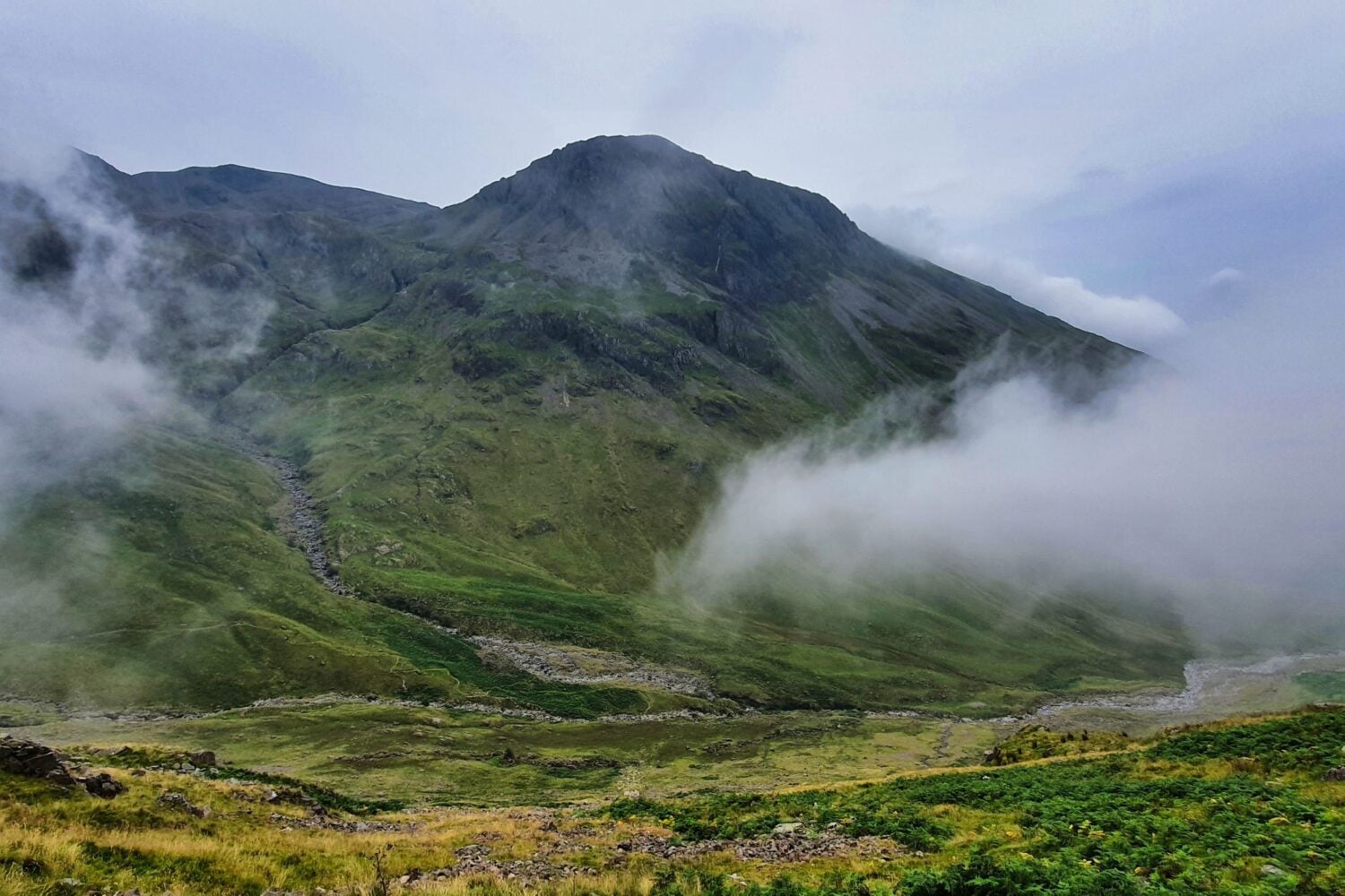 A view of a green covered mountain with misty clouds in the foreground.