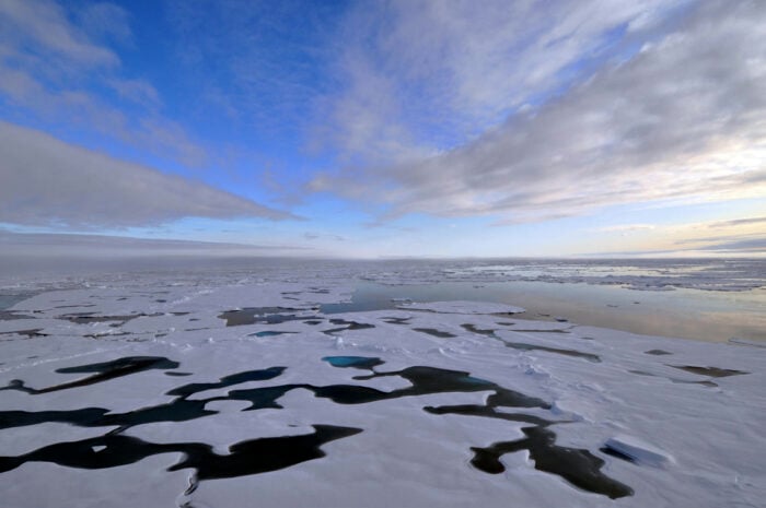 A view of the Arctic Ocean and sky. Sea ice is floating on top of the ocean.
