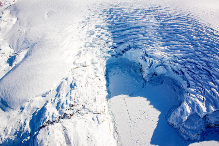 Photo taken from an aircraft looking down at a heart-shaped glacier that is breaking off.