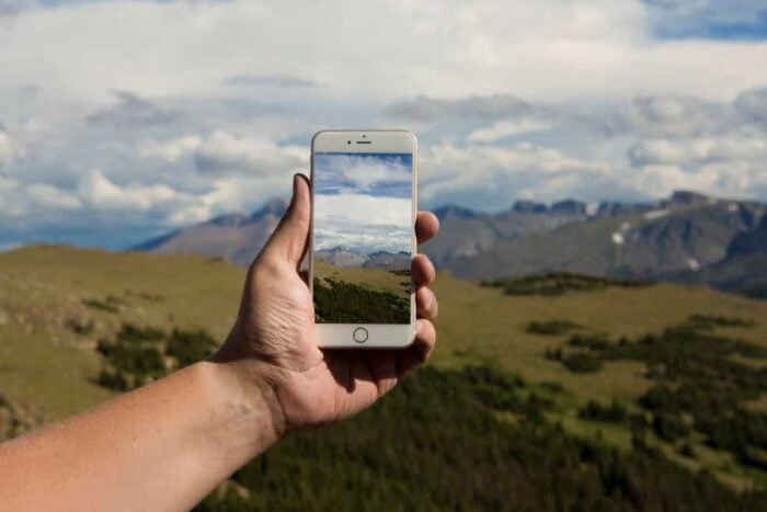 A picture of an arm holding a smartphone against the background of a hilly landscape with a picture of that landscape on the phone.