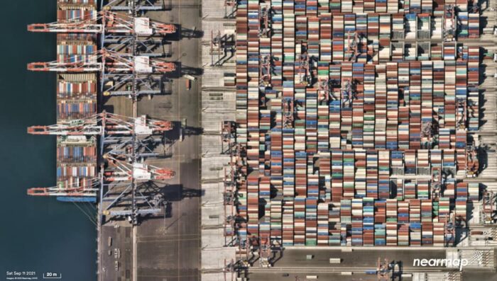 An aerial image of a port showing rows and rows of shipping containers. An edge of the ocean is the the left of the containers.