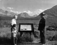 A black and white photo showing a park range, a white man in a white shirt, and a young girl wearing light color top and shorts in front of mountains and a prairie.