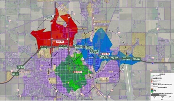 A faded aerial map with red, green, and blue areas indicating 3 minute drive times for a city.
