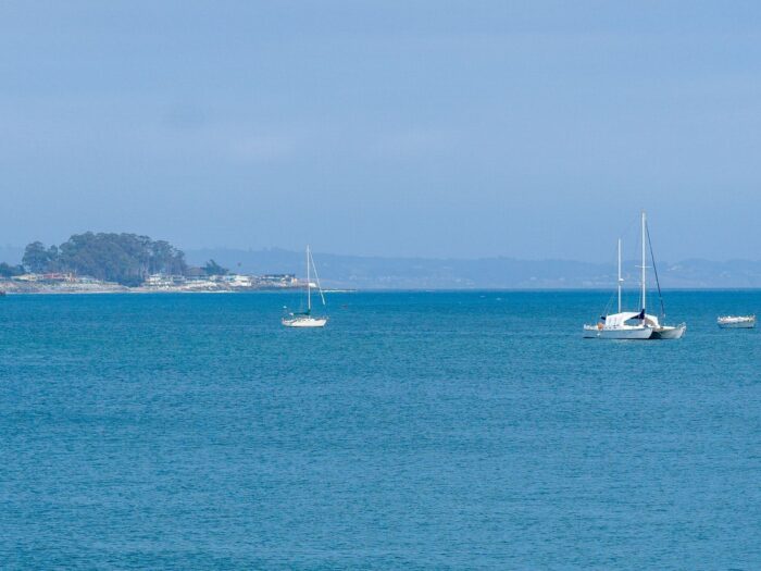 A couple of small white boats on a hazy day out in the ocean with the coastline in the background.