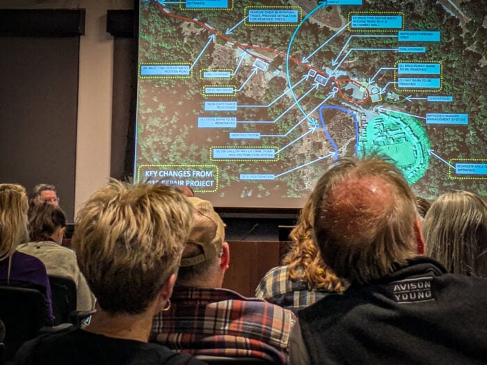 A group of people watching a presentation with a map on a screen.