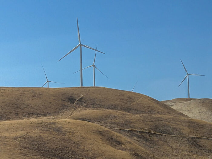 Wind mills on yellow grassy rolling hills in the bright sunshine.