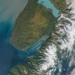 A satellite image of a peninsula with a turquoise lake.