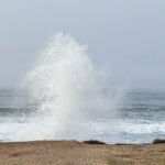 A photo of a wave spray against a cliff by the ocean.