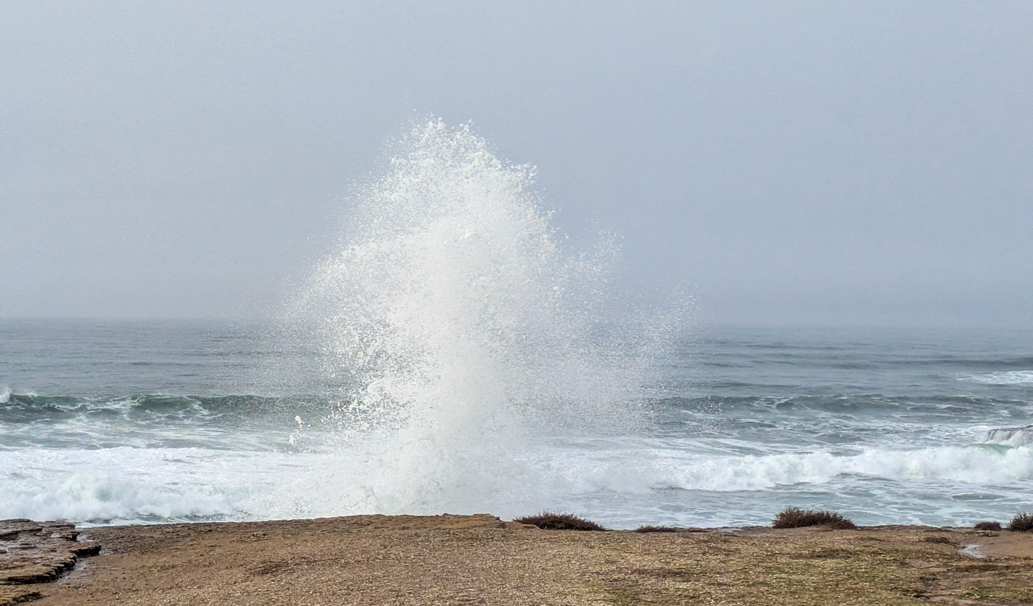 A photo of a wave spray against a cliff by the ocean.
